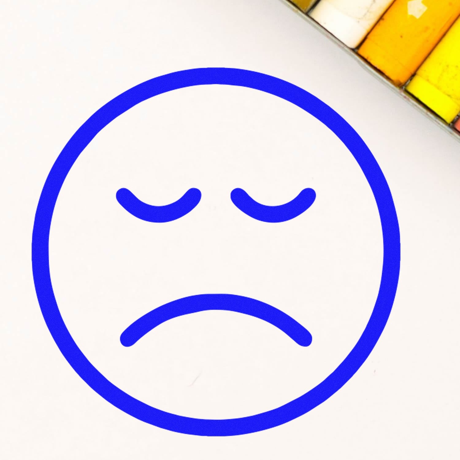 Wood Handle Downer Frown Emoticon Rubber Stamp imprint showing a blue frown face on white paper, with colored pencils in the background.