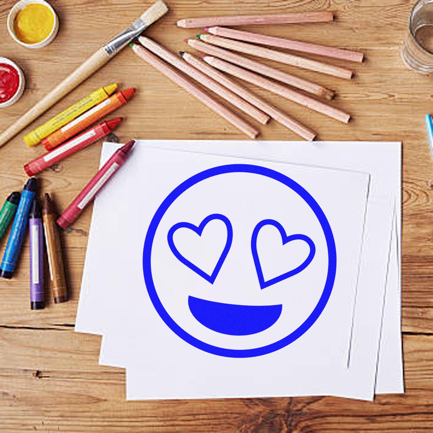 Self-Inking Heart-Eyes Reaction Stamp on paper, surrounded by colorful art supplies on a wooden table. Perfect for adding fun, expressive touches to crafts and stationery.