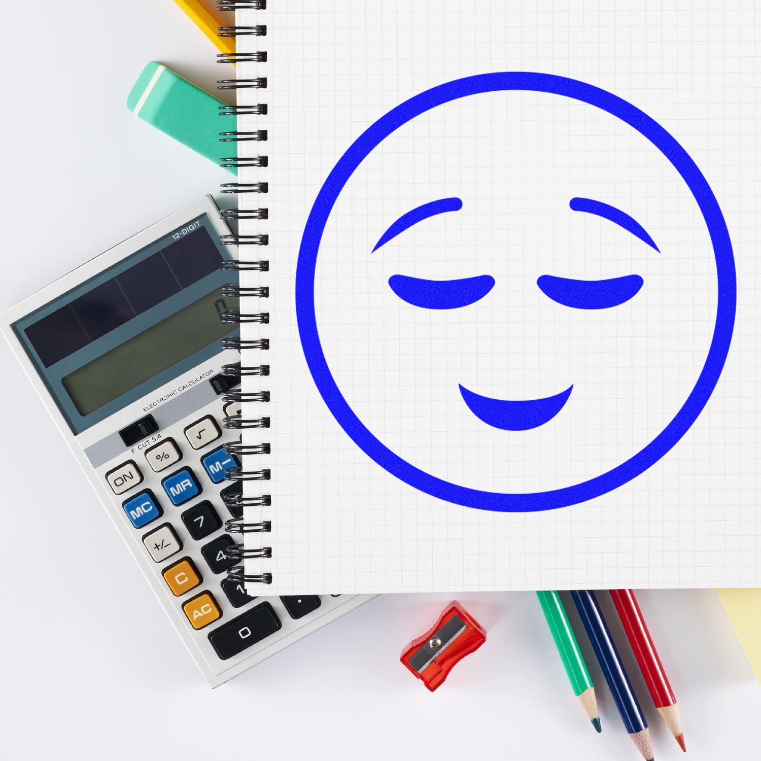 Self-Inking Contentment Facial Expressions Stamp on notepad, featuring a blue smiling face. Includes calculator, eraser, and colored pencils. Perfect for adding a cheerful touch to documents.