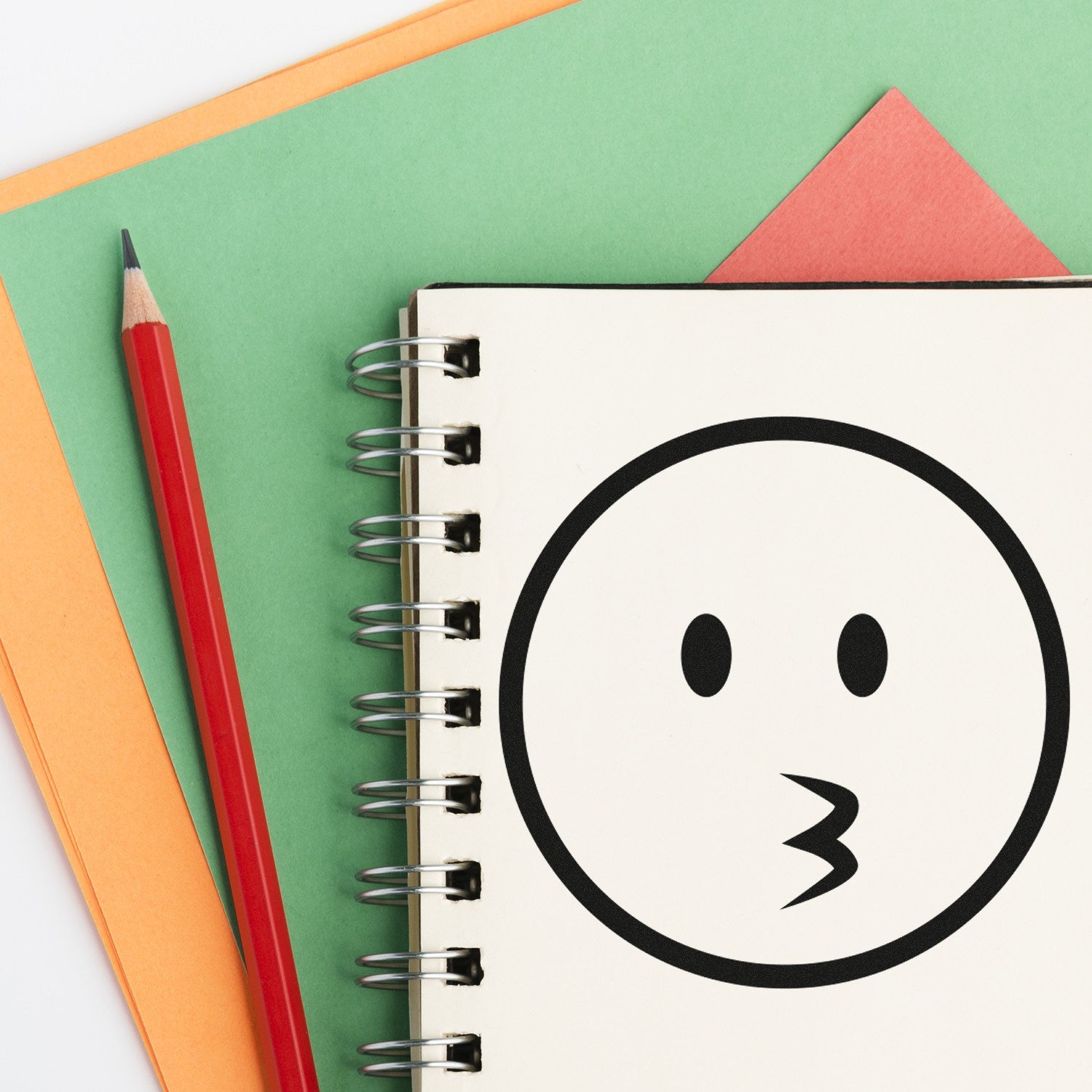 Wood Handle Whistling Wil Emojicons Rubber Stamp on a spiral notebook, featuring a whistling face design. Perfect for adding playful touches to stationery.