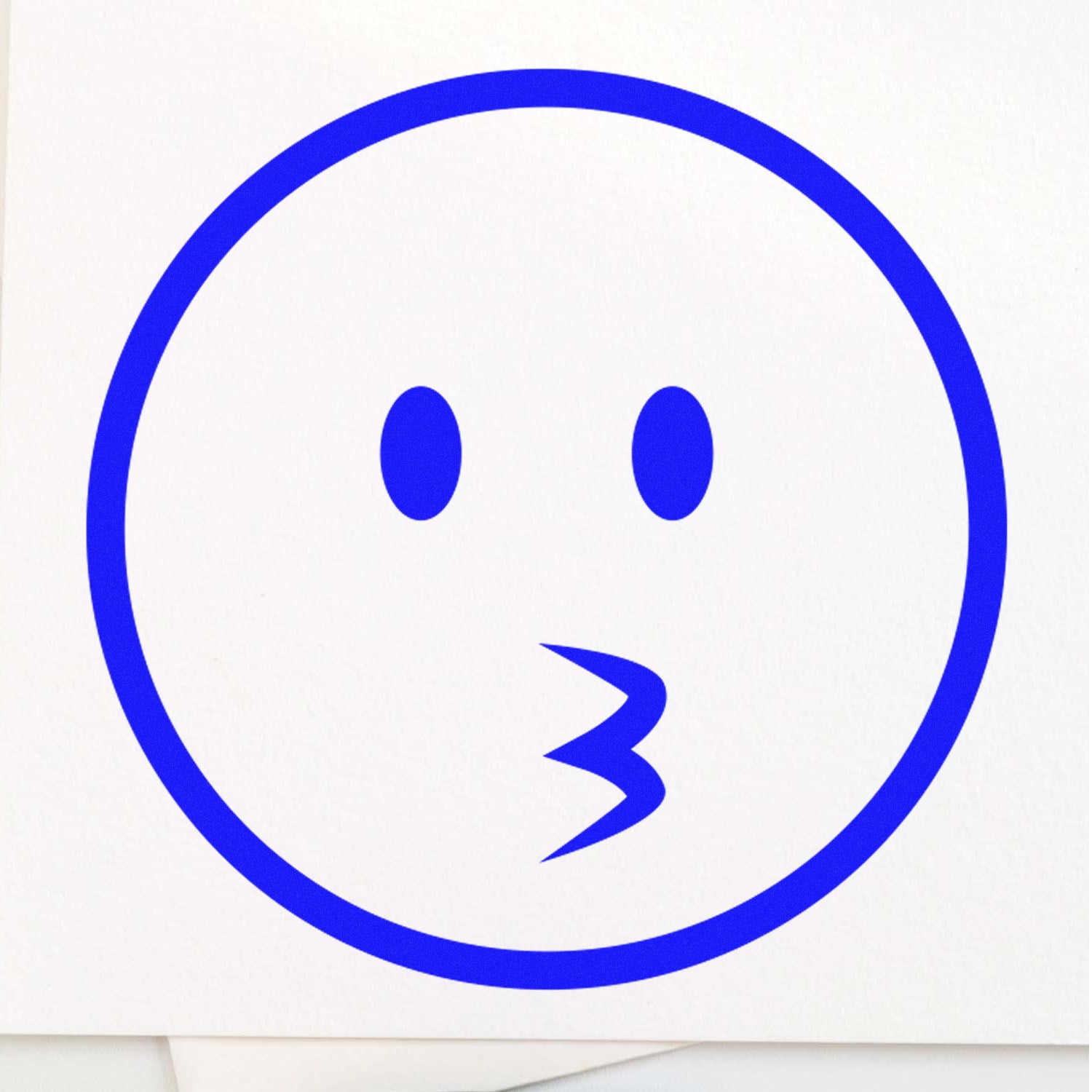 Wood Handle Whistling Wil Emojicons Rubber Stamp featuring a blue whistling face design on white paper. Perfect for adding playful expressions to crafts and stationery.