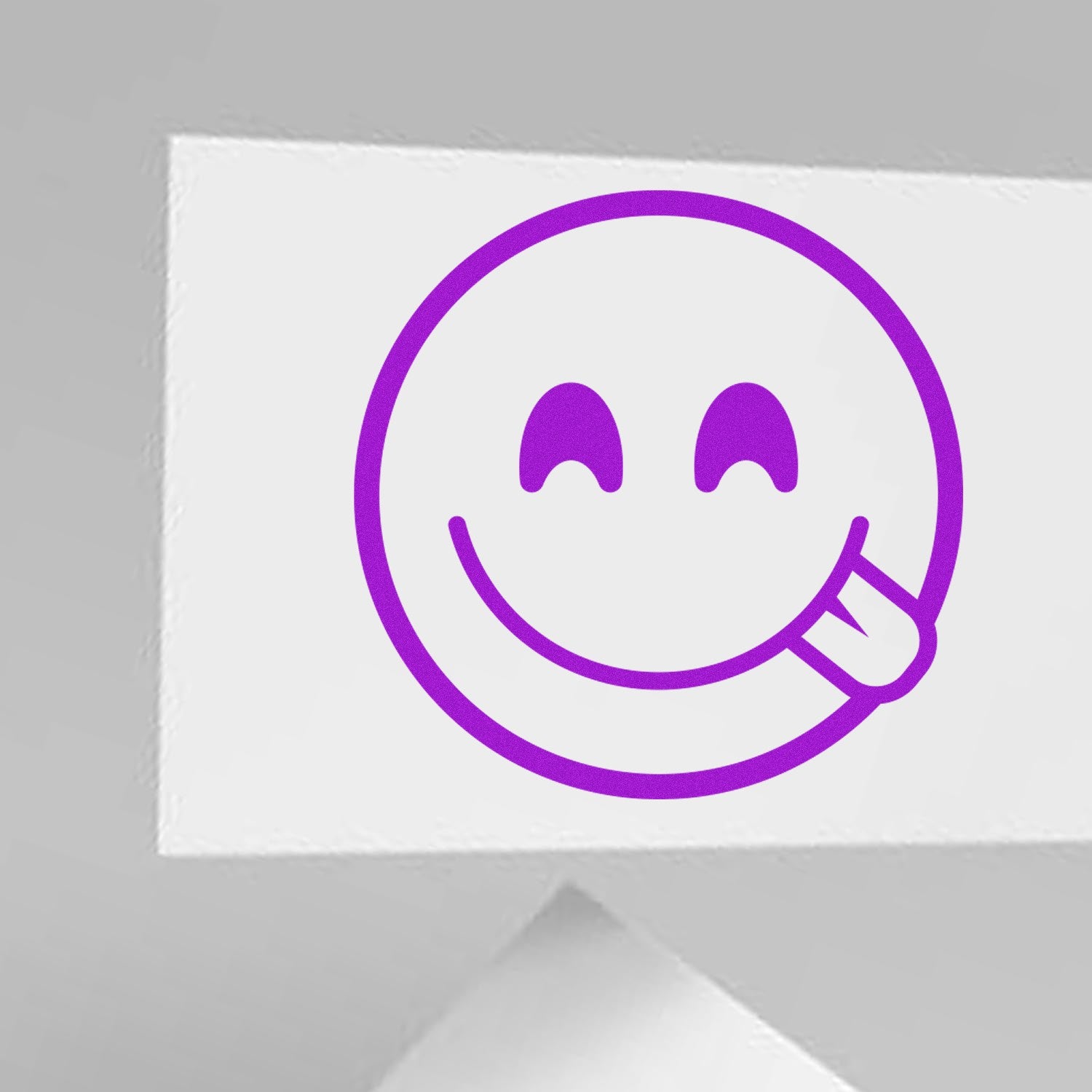 Wood Handle Cheeky Winky Emoji Rubber Stamp on white paper, featuring a playful purple winking face with tongue out. Perfect for adding fun to crafts and stationery.