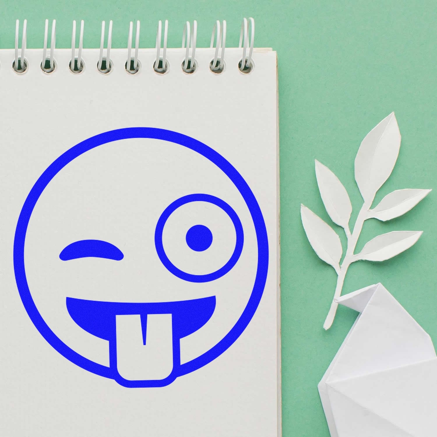 Self-Inking Goofy Wink Emoji Stamp on a notepad, featuring a playful blue emoji with a wink and tongue out, perfect for adding fun to your stationery.