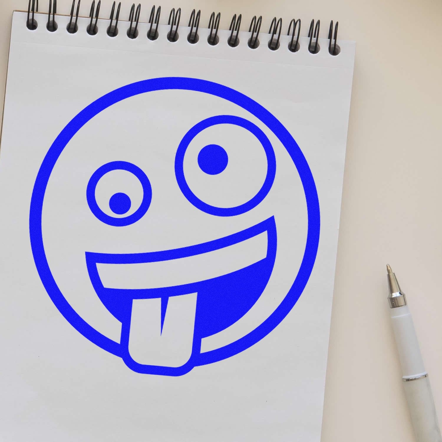 Self-Inking Zany Grin Emoji Stamp on a notepad, showcasing a playful blue emoji with a tongue out. Perfect for adding fun to notes and crafts.