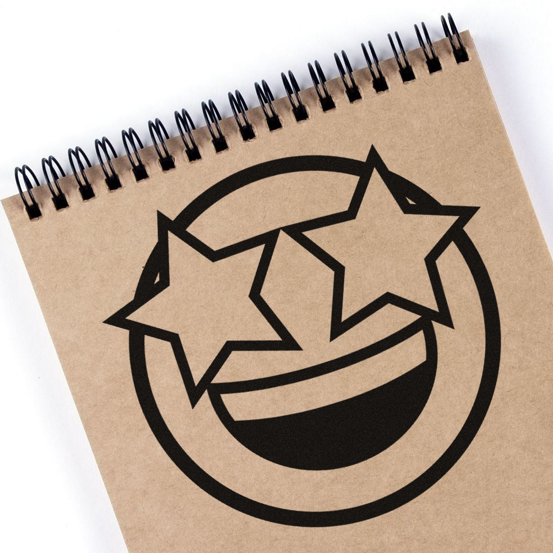 Self-Inking Starry Eyed Emotes Stamp imprint on a spiral notebook, featuring a smiling face with star-shaped eyes. Perfect for adding fun, expressive designs to your stationery.