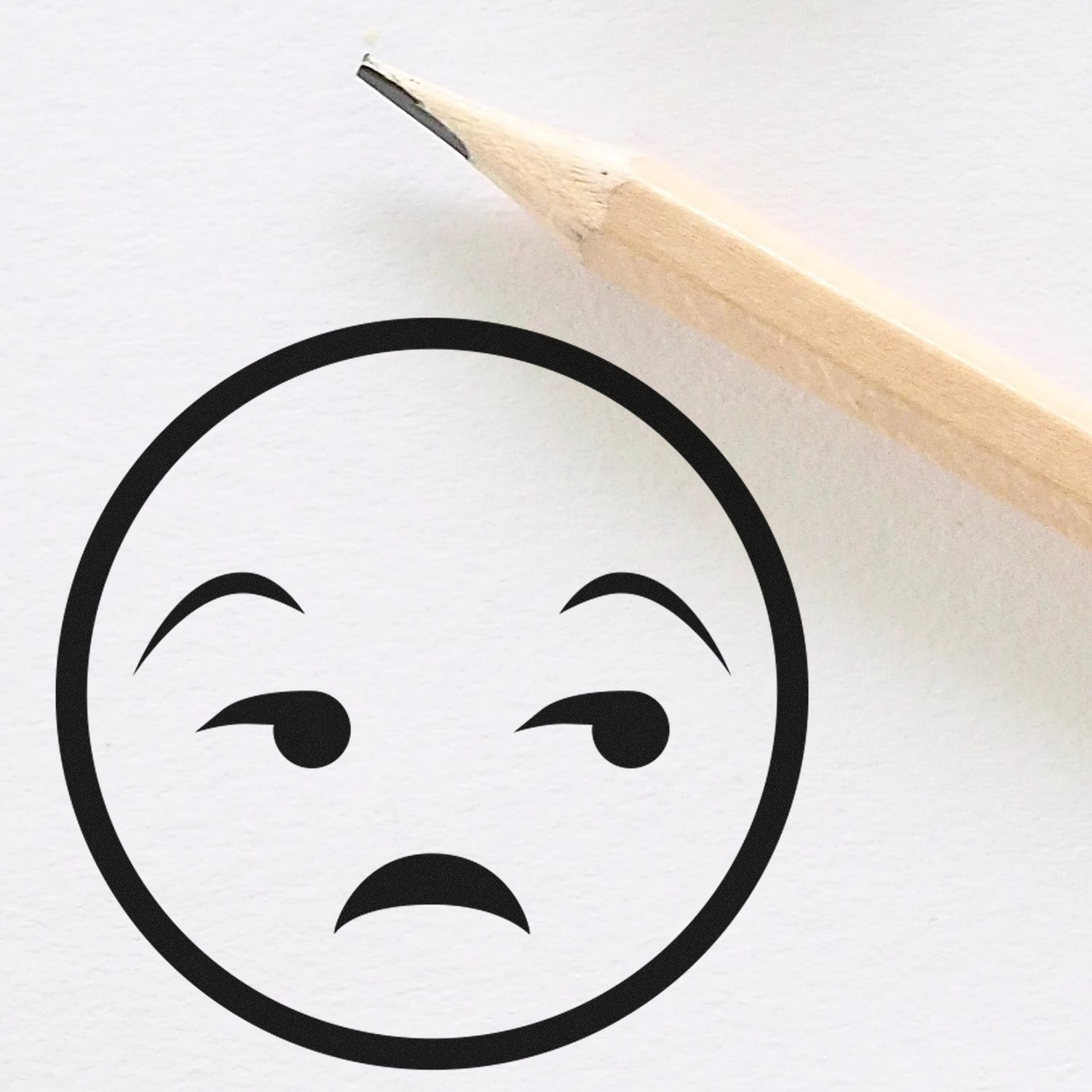 Self-Inking Grumpy Gus Facial Expressions Stamp creating a skeptical face on white paper, next to a wooden pencil.