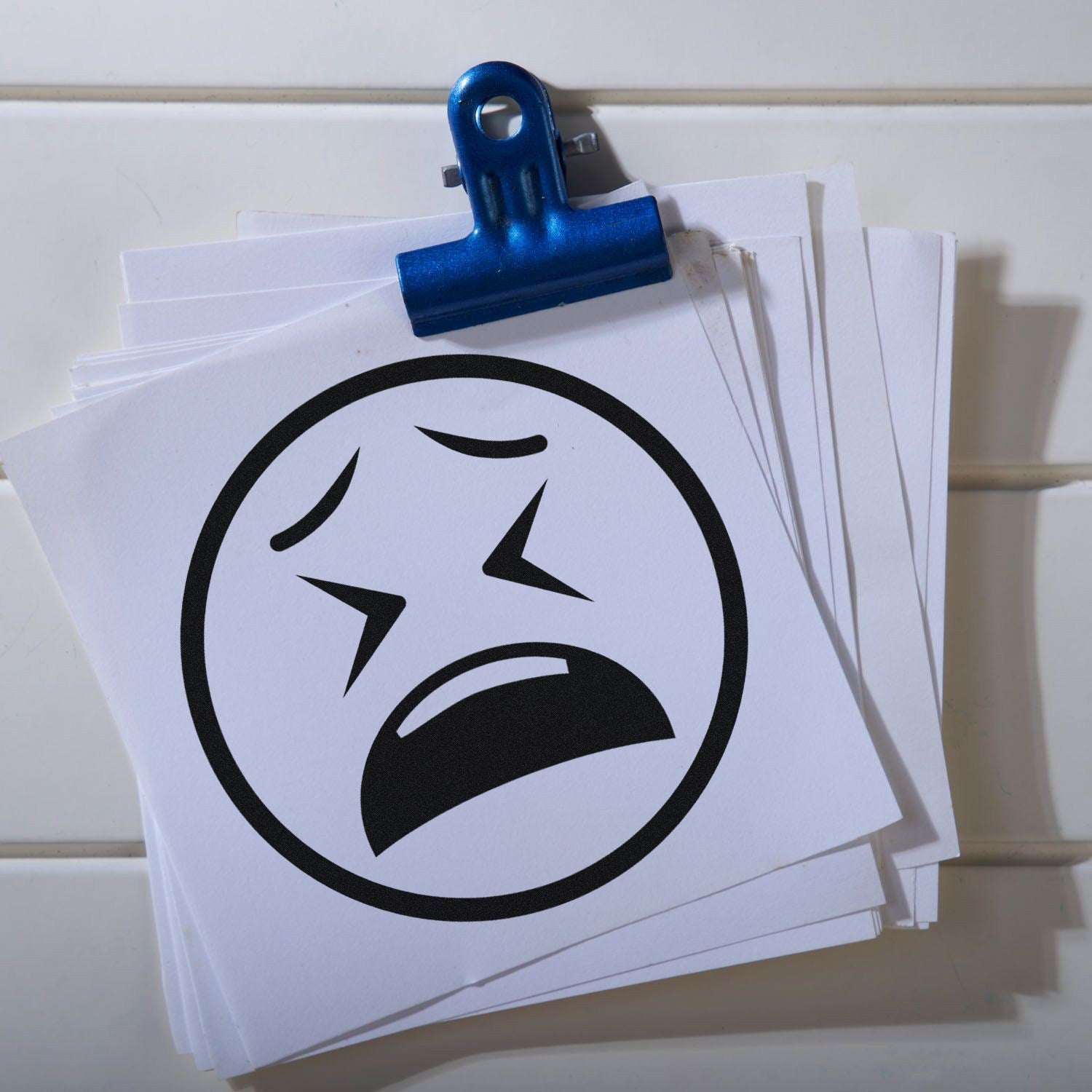 Self-Inking Clenched Cry Emoji Stamp on white paper stack, featuring a distressed face with clenched eyes and mouth. Perfect for adding expressive flair to documents and crafts.