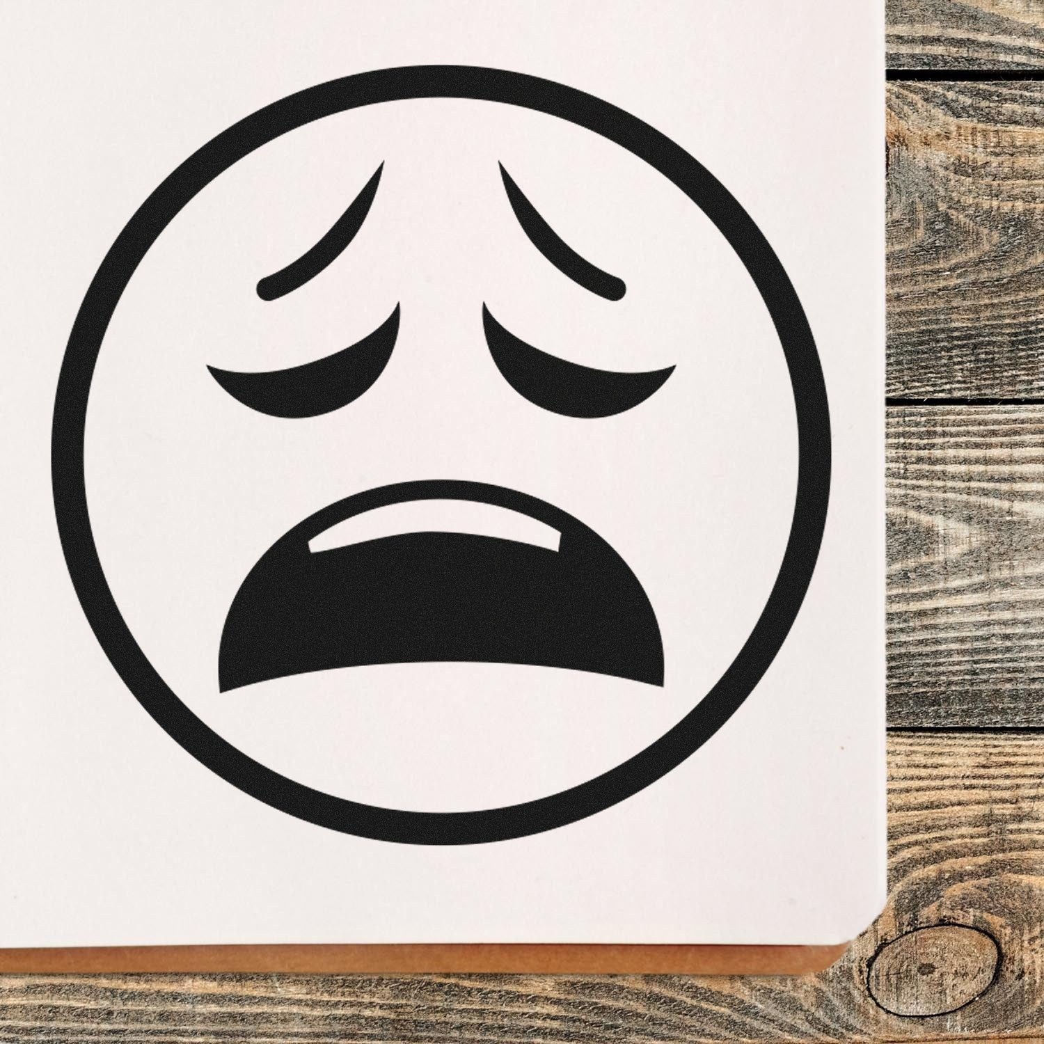 Self-Inking Cry of Despair Emoji Stamp on wooden surface, featuring a black, distressed face with furrowed brows and open mouth, perfect for adding expressive flair to documents and crafts.