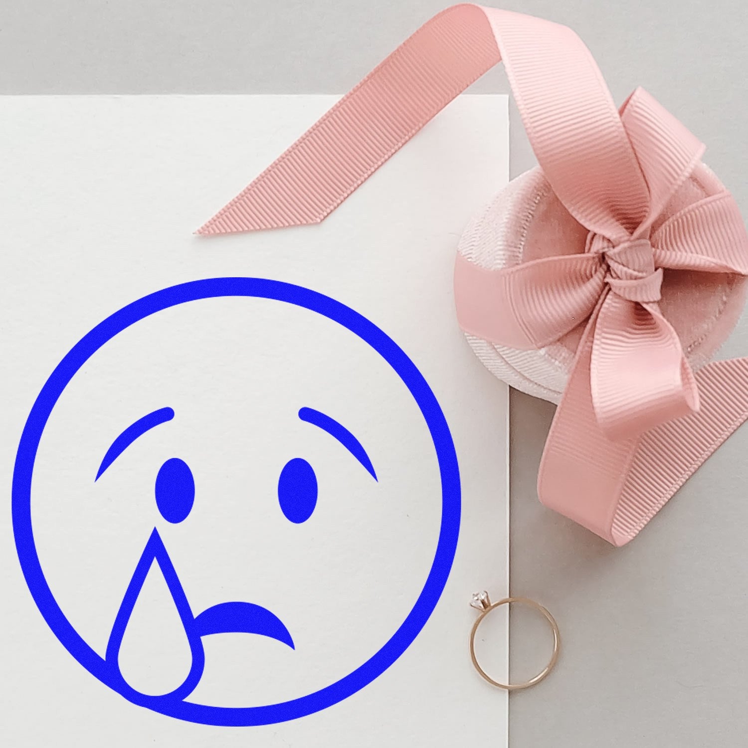 Wood Handle Teary Timmy Emoji Rubber Stamp on paper, featuring a blue teary-eyed emoji. Perfect for crafts and stationery. Includes a pink ribbon and a ring for decorative touch.