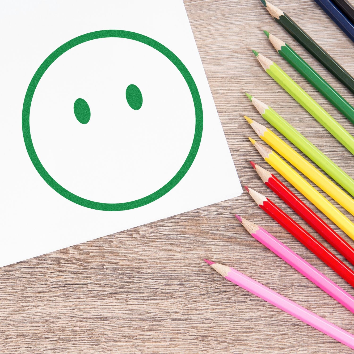 Self-Inking Speechless Sam Emoji Stamp on paper, surrounded by colorful pencils on a wooden surface. Perfect for adding fun, expressive touches to crafts and documents.