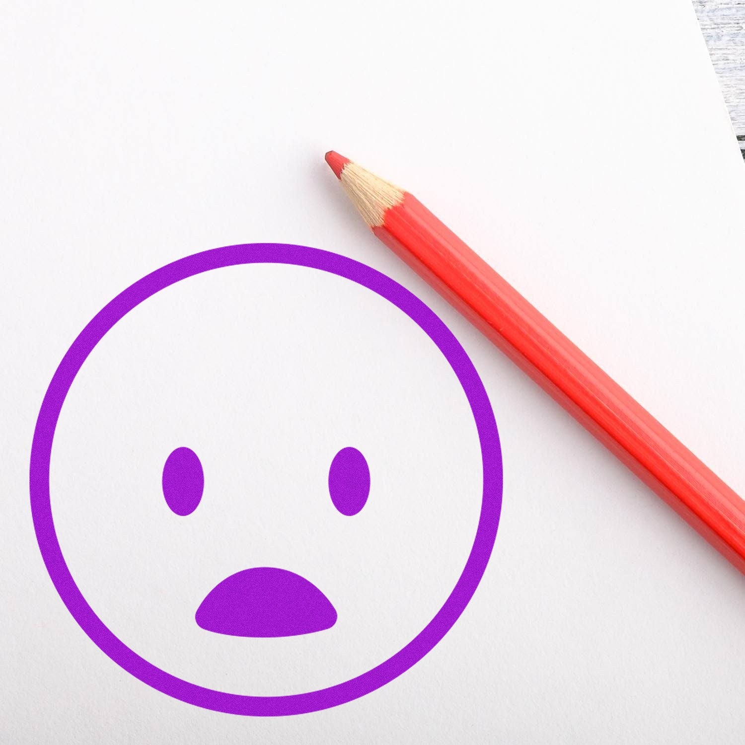 Wood Handle Surprised Smiley Emoji Rubber Stamp imprint in purple on paper, next to a red pencil. Perfect for adding fun expressions to crafts and stationery.