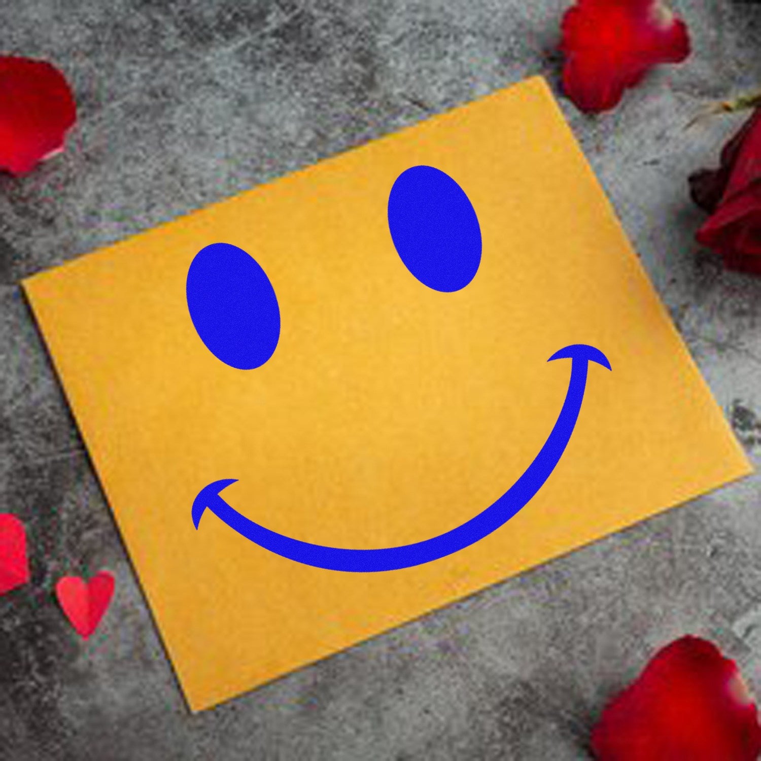 Self-Inking Cheeky Smirk Emoji Stamp on yellow paper, surrounded by red rose petals. Perfect for adding a playful touch to notes and crafts.