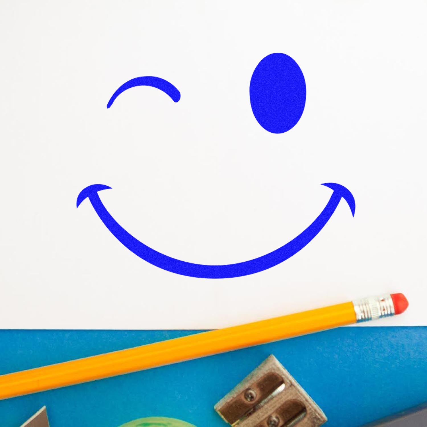 Wood Handle Winky Smirk Emoji Rubber Stamp imprint on white paper, featuring a playful blue winky face. Includes a pencil and sharpener for scale. Perfect for crafts and stationery.