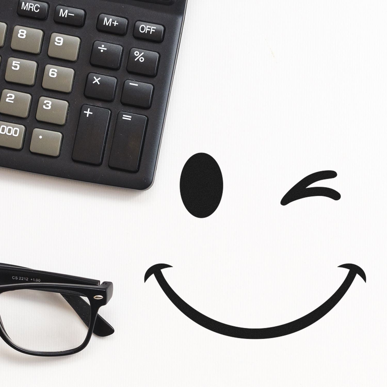 Self-Inking Winky Smiley Emoji Stamp on white paper, next to a calculator and glasses. Perfect for adding a playful touch to documents and crafts.