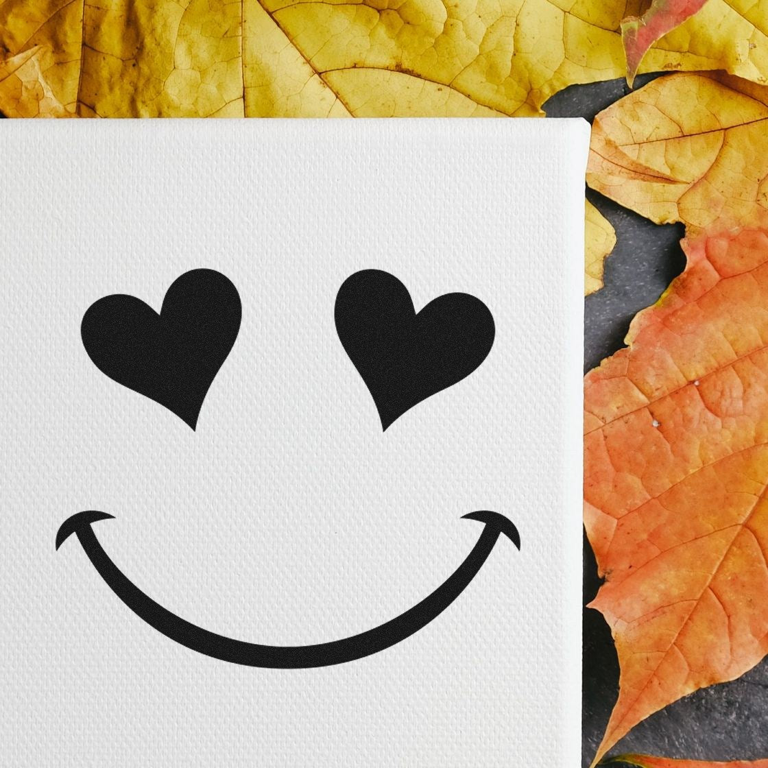 Wood Handle Heart Eyes Delight Emoticon Rubber Stamp on canvas, featuring a smiling face with heart-shaped eyes, surrounded by autumn leaves. Perfect for crafting and personalizing projects.