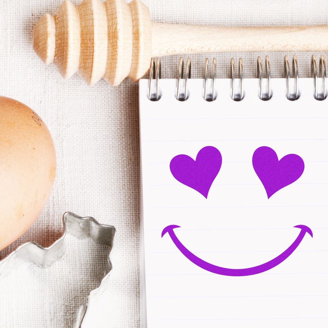 Wood Handle Heart Eyes Delight Emoticon Rubber Stamp on notepad, featuring a purple heart-eyed smiley face. Perfect for crafts and stationery enthusiasts.