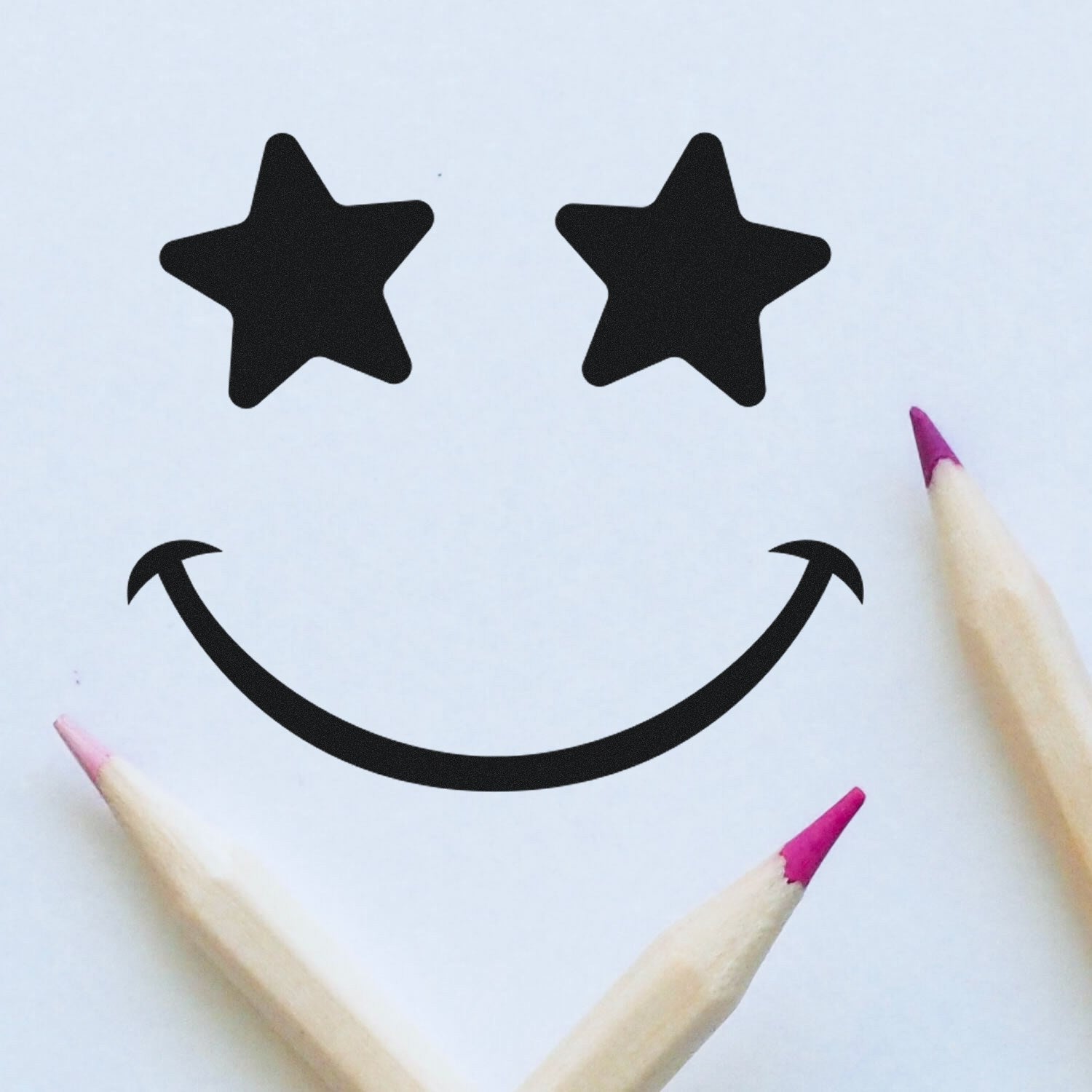 Self-Inking Starstruck Smile Smiley Stamp with star eyes and a curved smile, shown on white paper with pink-tipped pencils. Perfect for adding fun, expressive designs to your projects.