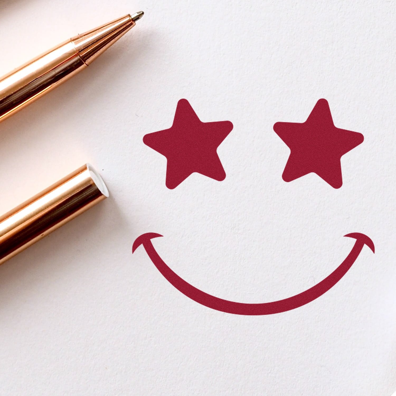 Wood Handle Starstruck Smile Smiley Rubber Stamp imprint showing a smiley face with star eyes, next to a gold pen on white paper. Perfect for adding a playful touch to crafts.