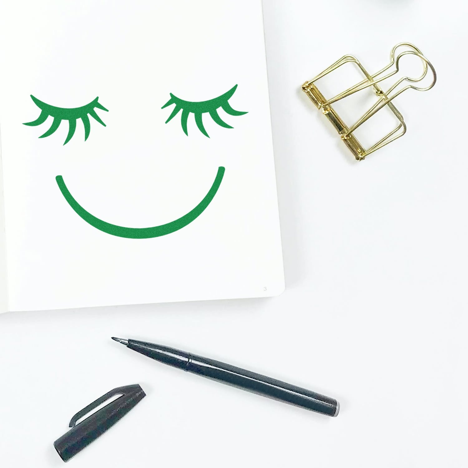 Self-Inking Dreamy Delight Pictogram Stamp creating a green smiling face with closed eyes on white paper, alongside a black pen and gold paper clip.