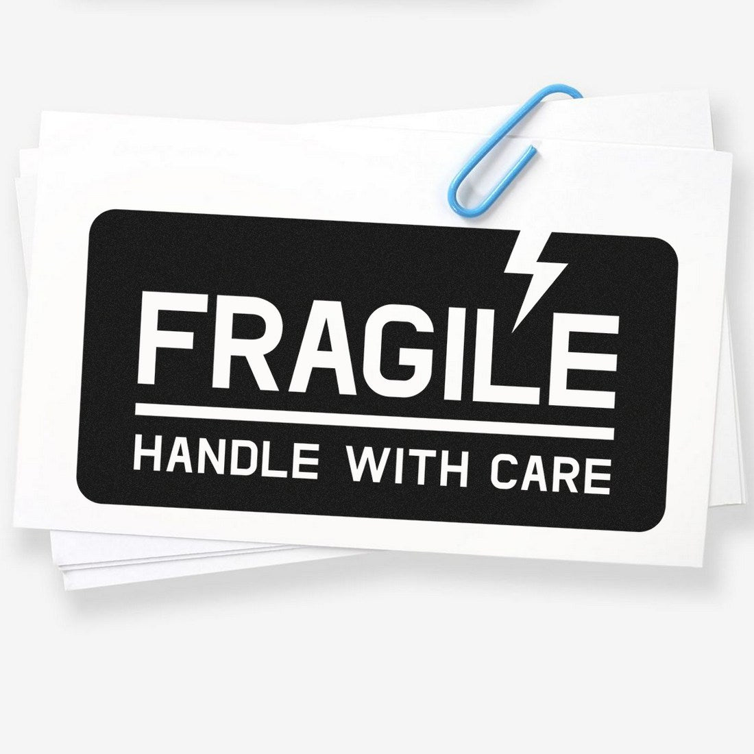 PSI Pre-Inked Lightning Fragile Stamp with bold 'Fragile Handle with Care' text and lightning icon, ideal for marking packages. Black and white design on a stack of papers with a blue paperclip.