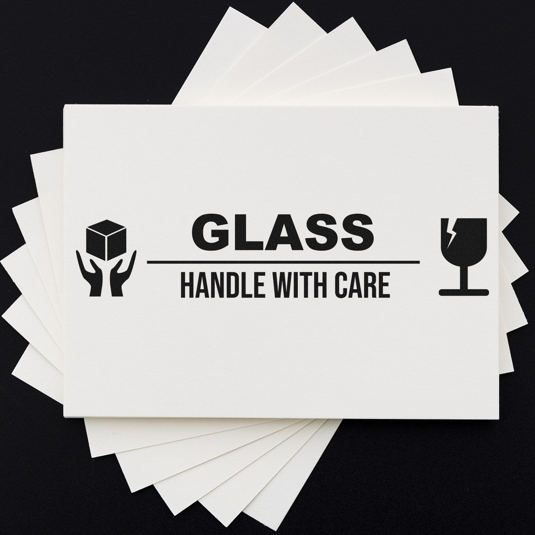 Image of a Slim Pre-Inked Glass Handle With Care Stamp, featuring bold black text and icons of a fragile glass and hands holding a box, on a white card background. Ideal for packaging use.