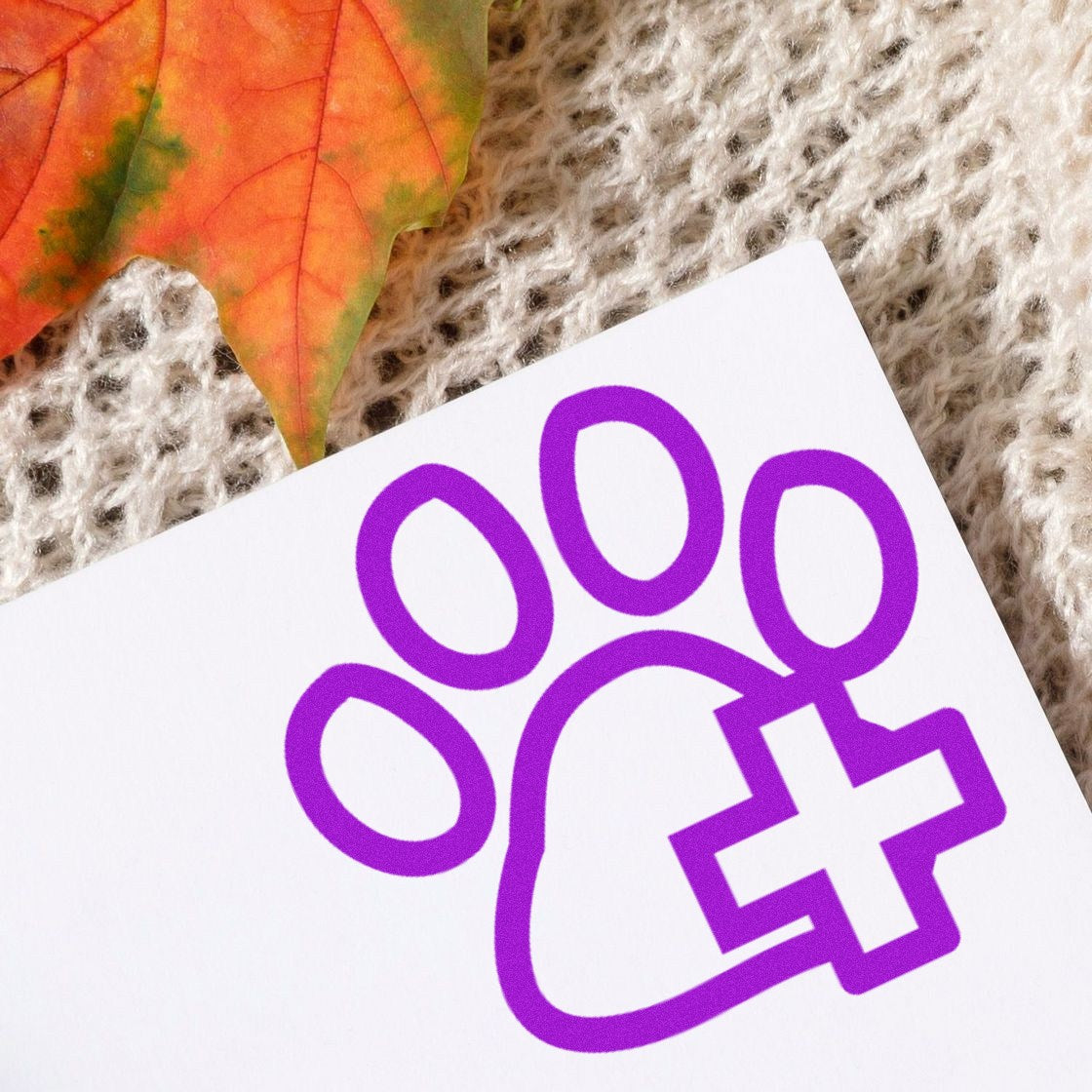 Wood Handle Healthy Pet Frequent Buyer Rubber Stamp with a purple paw print and cross design, placed on a textured surface with an autumn leaf nearby. Perfect for pet loyalty programs.