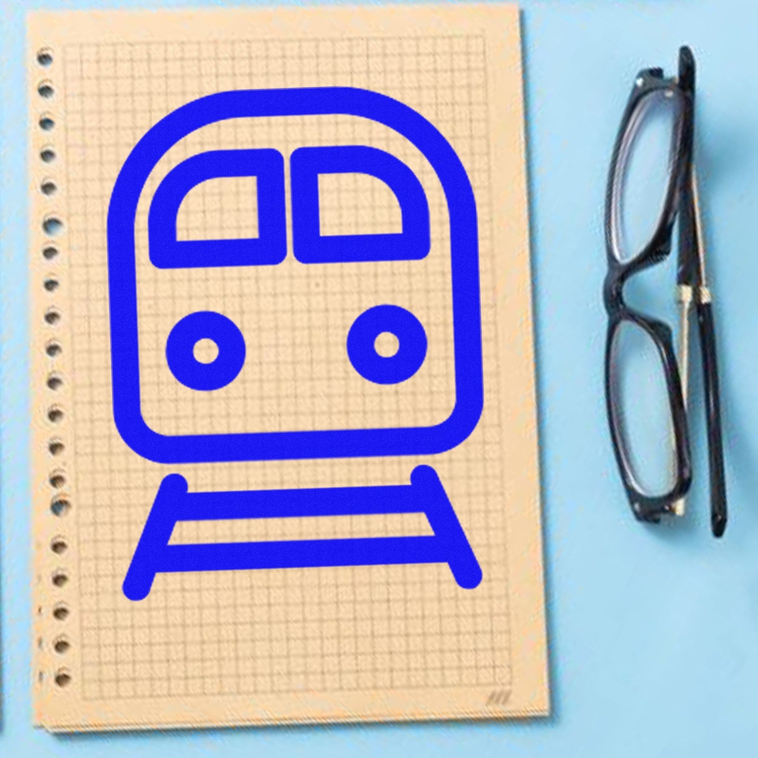 Wood Handle Happy Railways Loyalty Scheme Rubber Stamp on graph paper, featuring a blue train design. Glasses placed beside the paper on a light blue background.