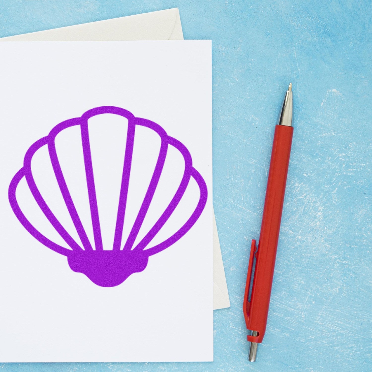 Self-Inking Beach Beauty Membership Stamp featuring a vibrant purple seashell design on a card, with a red pen nearby, set against a textured blue background.