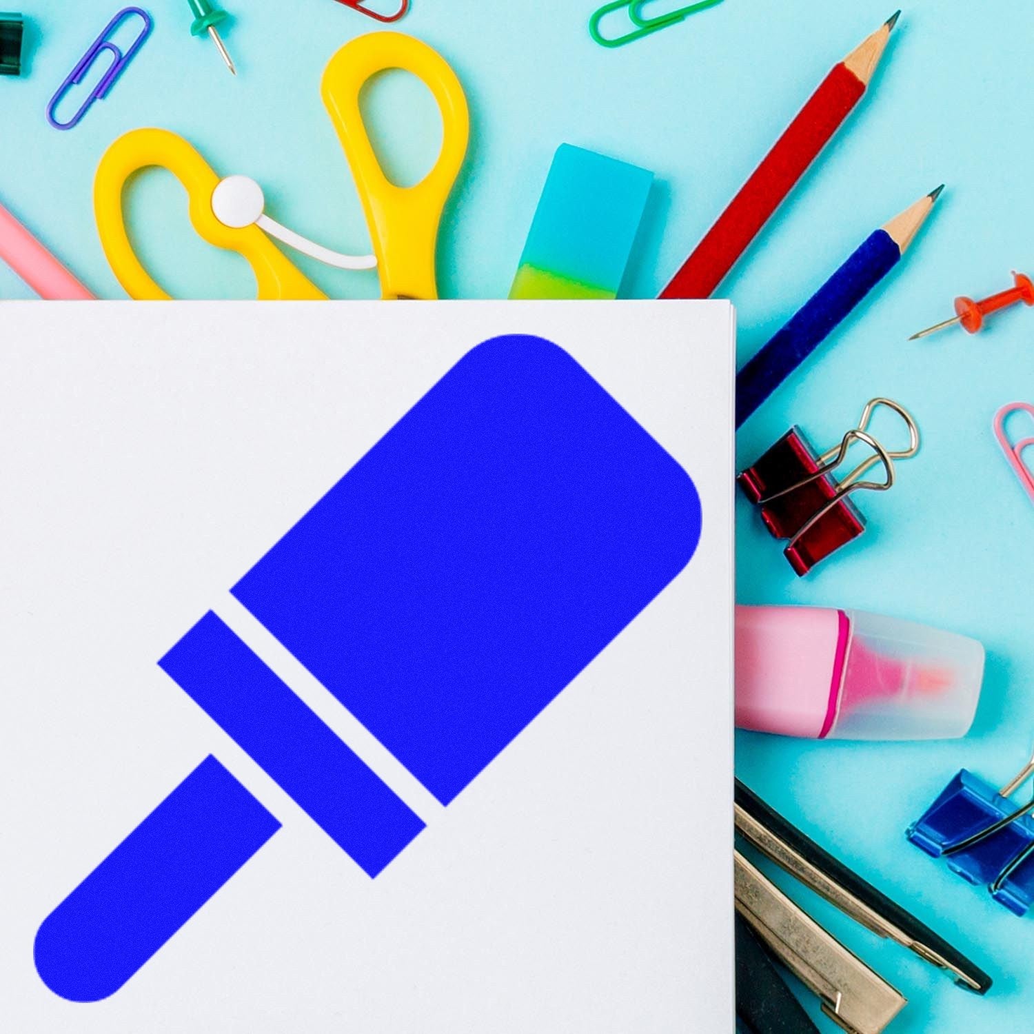 Self-Inking Pop Of Approval Visit Stamp with a bold blue popsicle design, surrounded by colorful office supplies on a light blue background.