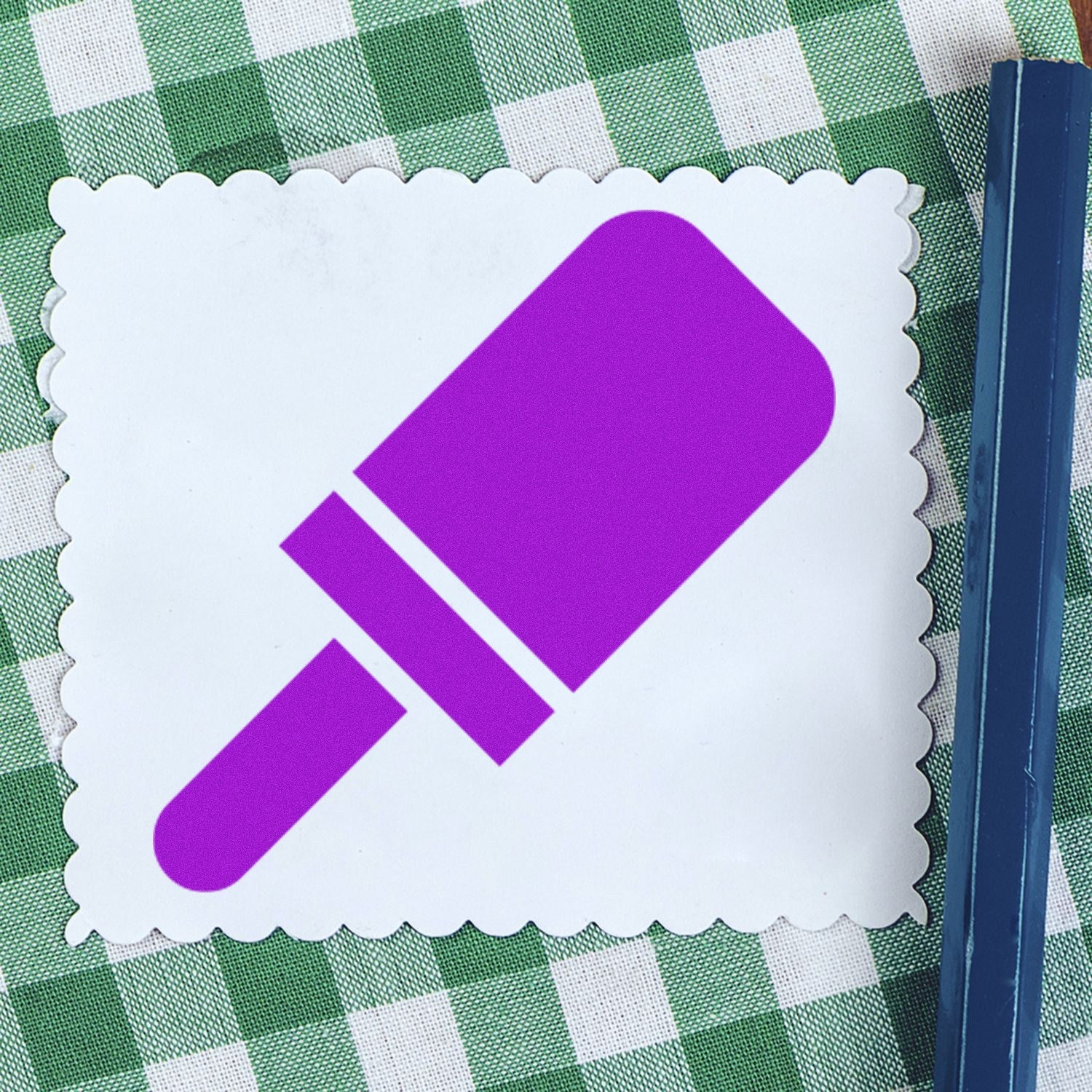 Wood Handle Pop Of Approval Visit Rubber Stamp on a green checkered tablecloth, featuring a purple popsicle design on a white scalloped card.