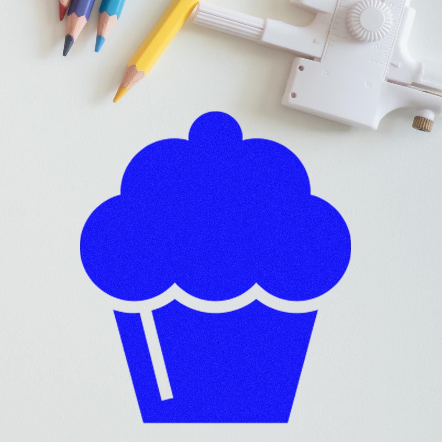 Self-Inking Cupcake Delight Loyalty Stamp with a blue cupcake design, shown on a light background with colored pencils and a compass nearby.