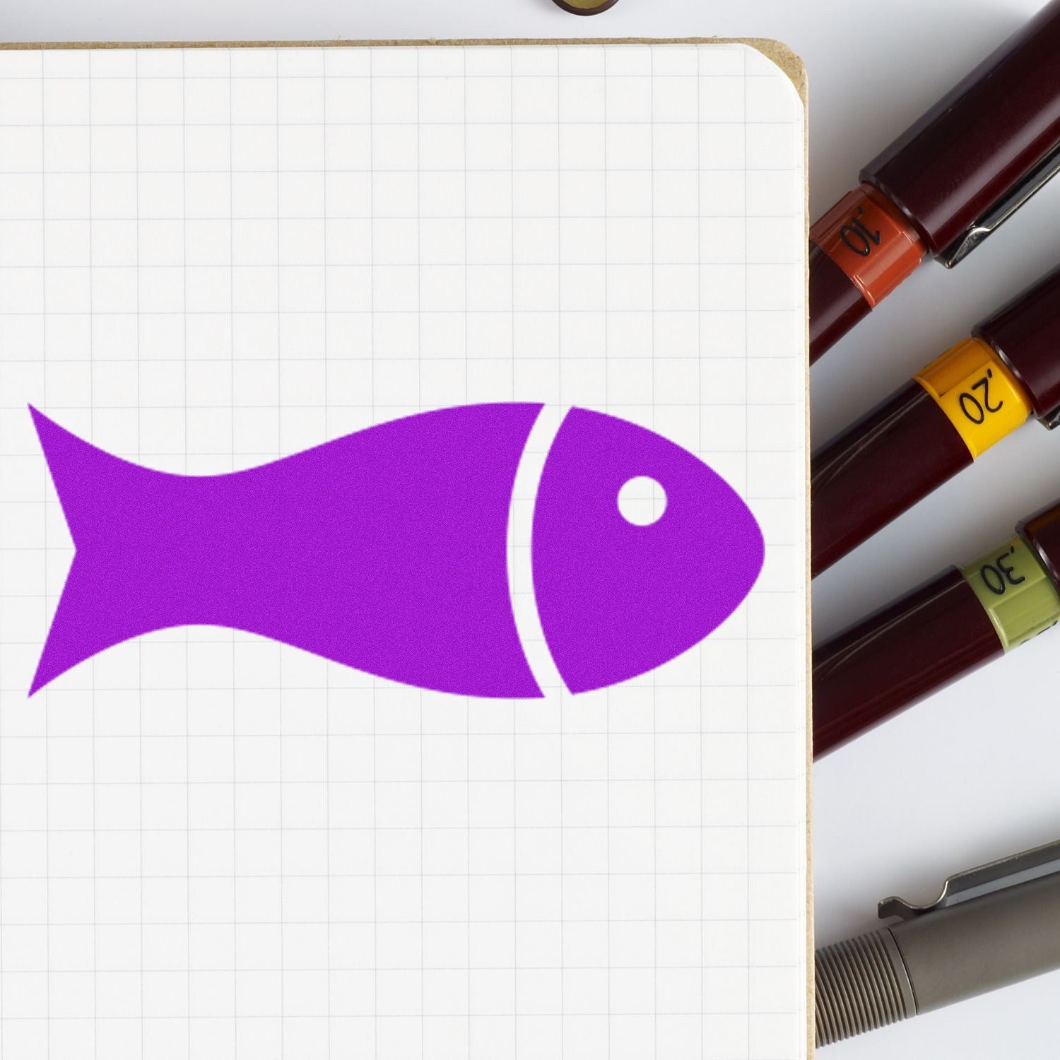 Wood Handle Fin-Tastic Loyalty Incentive Rubber Stamp featuring a purple fish design on a grid notebook, surrounded by colorful pens. Perfect for creative projects and rewards.