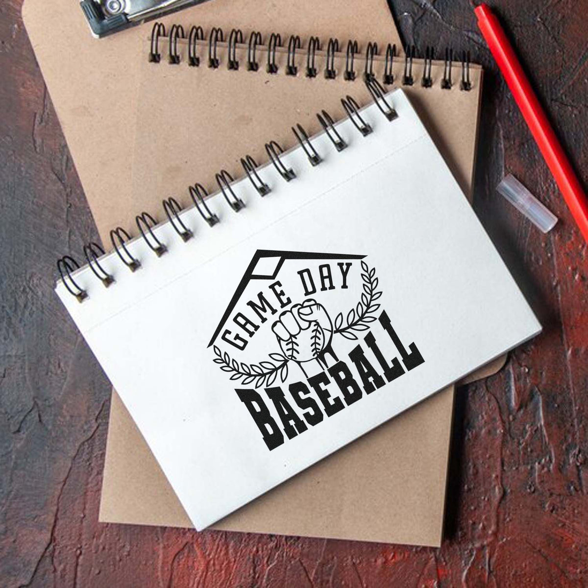 Black custom stamp and seal for baseball, reading Game Day Baseball, with fist and laurel wreath on white notebook.
