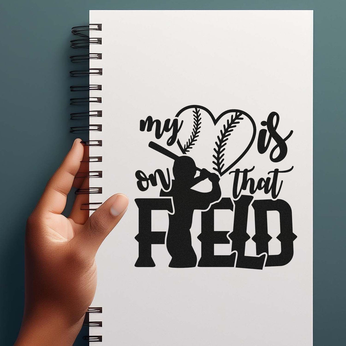 Black softball stamp/seal design on white spiral notebook, reading my heart is on that field with catcher silhouette.
