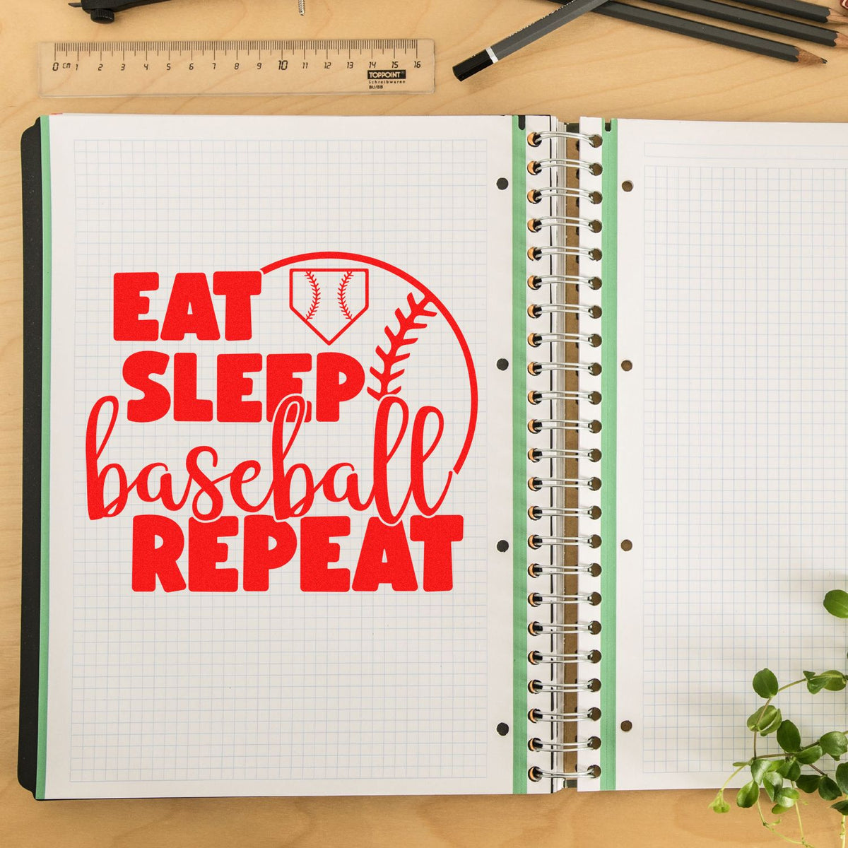 Red custom stamp seal reading EAT SLEEP baseball REPEAT on an open graph notebook with spiral binding.