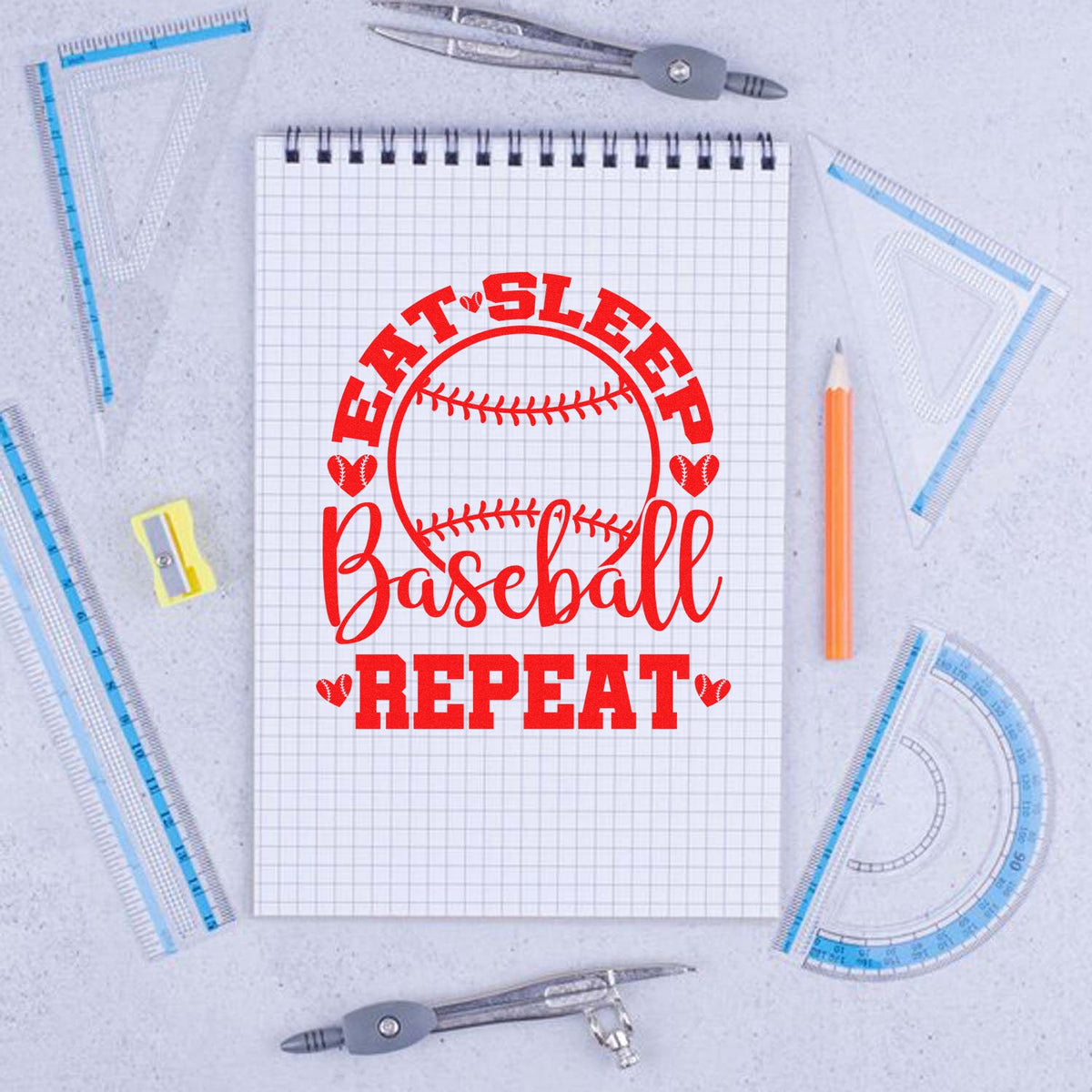 Red baseball heart stamp seal on graph notebook, surrounded by drafting tools and pencil on light gray background.