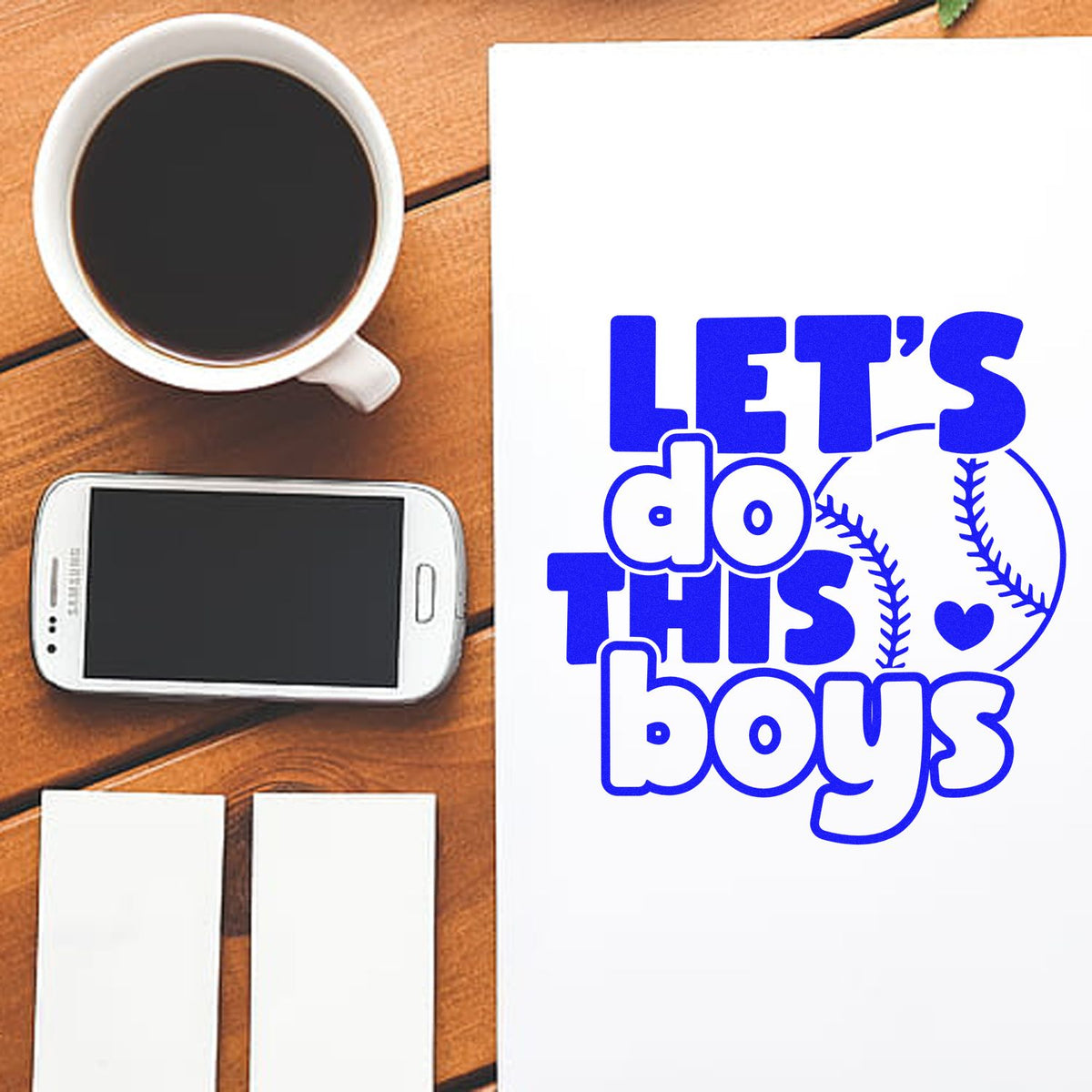 White stamp and seal products on a wooden table beside coffee and a phone, with a blue baseball-themed Lets do this boys design.