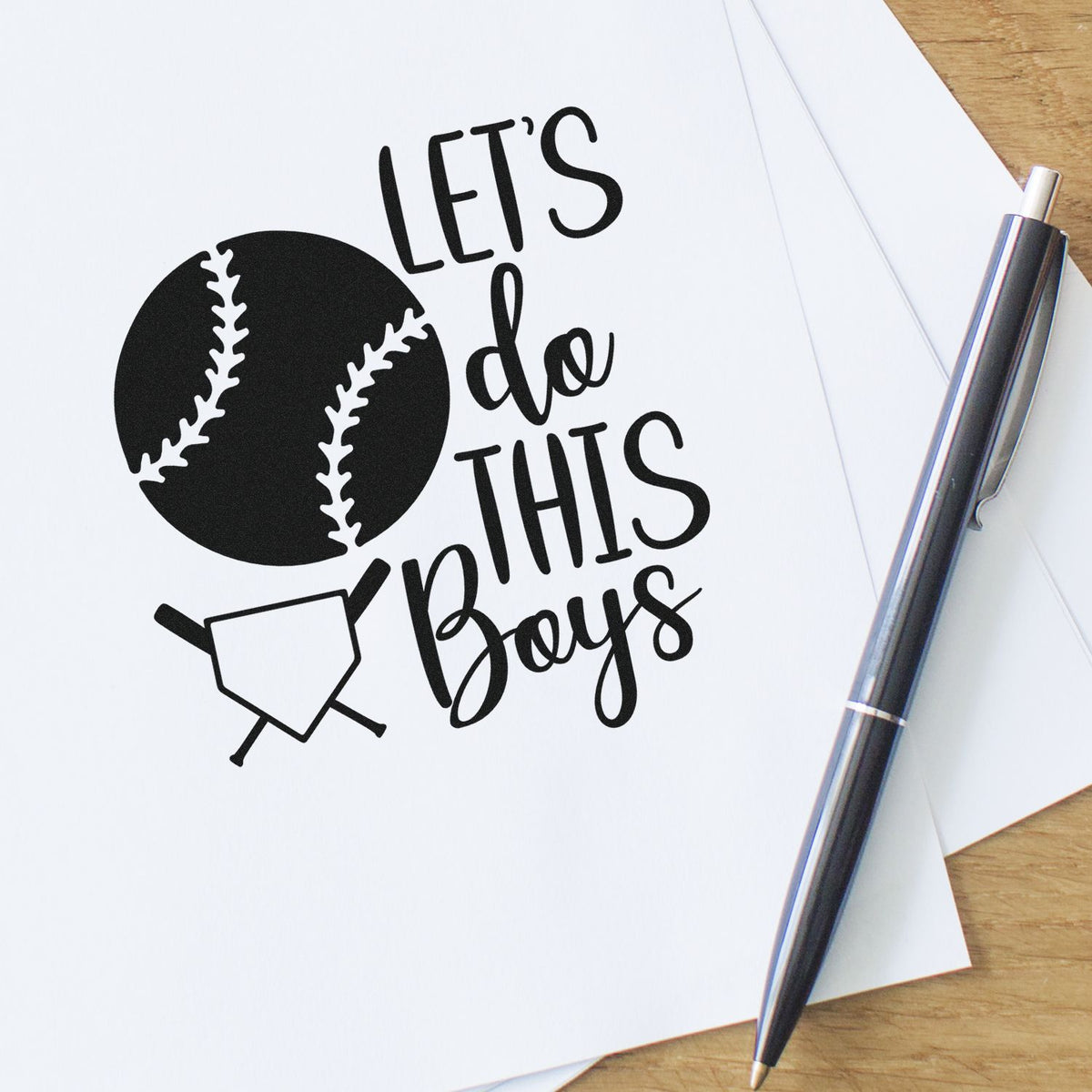 Black baseball-themed custom stamp and seal reading Lets do this Boys with baseball and home plate, beside a silver pen.