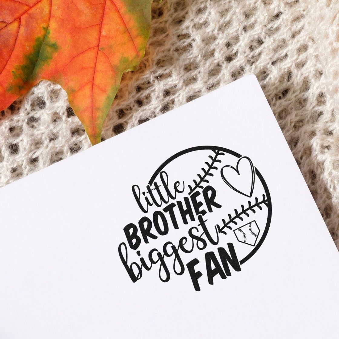 Black baseball-themed custom stamp seal reading little brother biggest fan on white paper, with heart and stitching details.