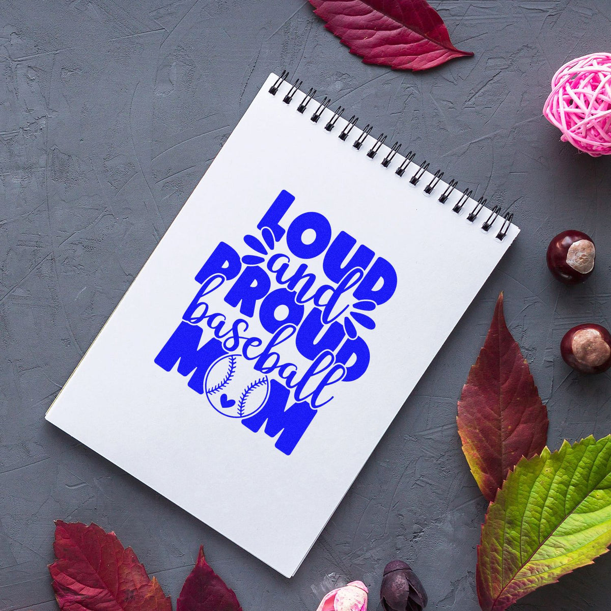 Blue Loud and Proud Baseball Mom stamp and seal design on a white spiral notebook, with baseball graphic on gray background.