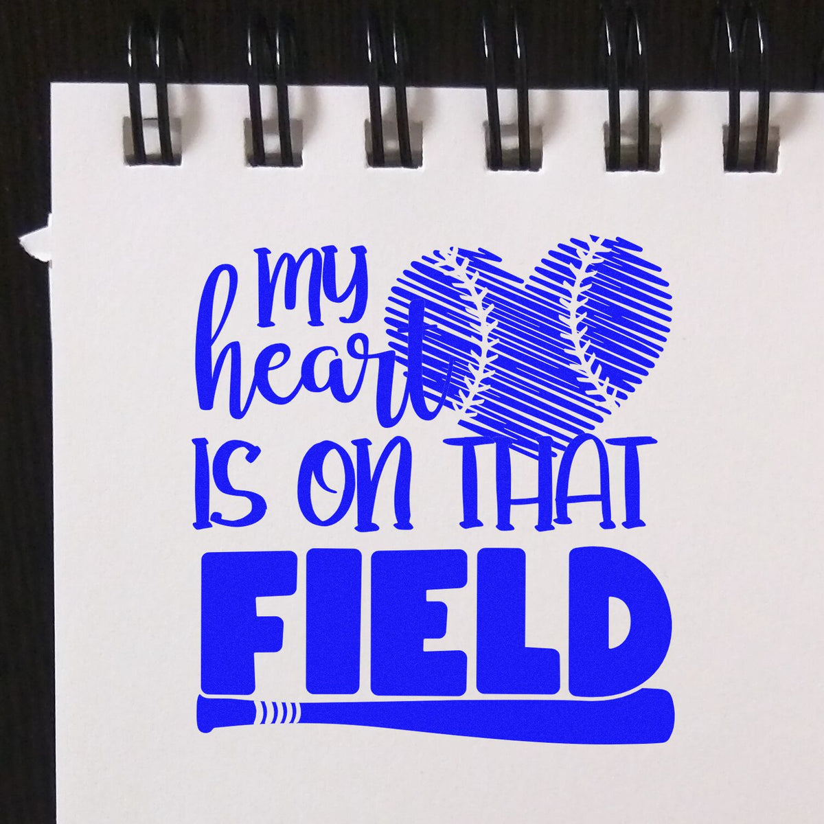 Blue softball custom stamp design reading my heart is on that field with heart-shaped ball and bat on white paper.