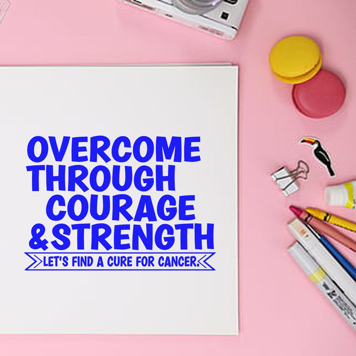 White card with blue cancer-awareness slogan on pink background, beside colorful stamp and seal products, markers, and clips.