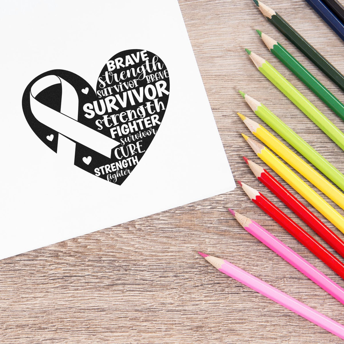 Black heart-shaped cancer awareness rubber stamp and seal with ribbon and words brave, survivor, strength, beside rainbow pencils.