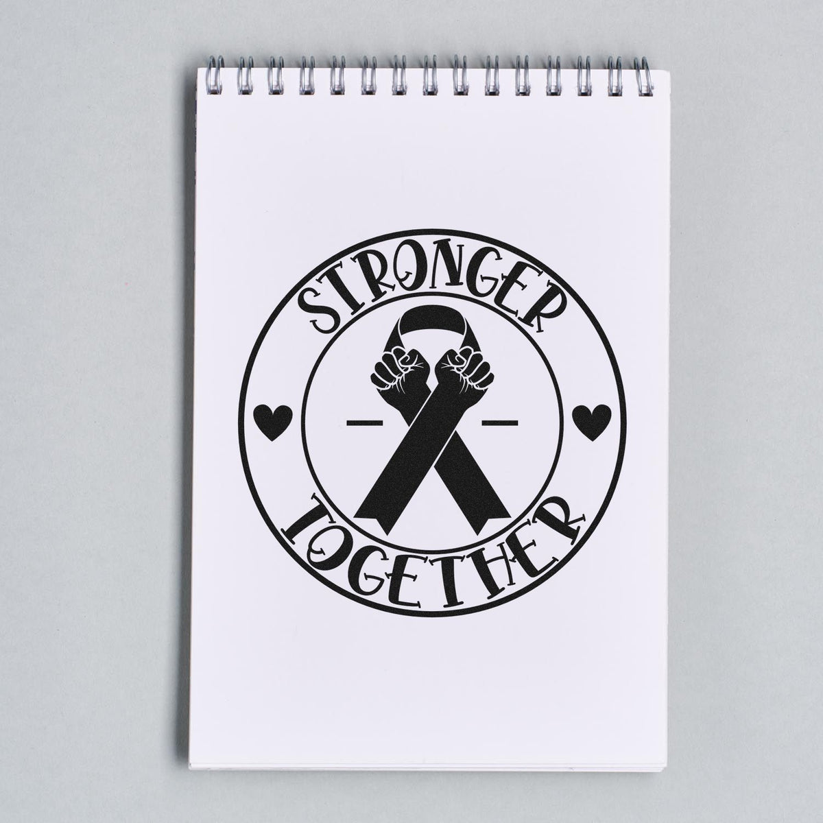 Black Stronger Together stamp and seal with raised fists and hearts on a white spiral notebook