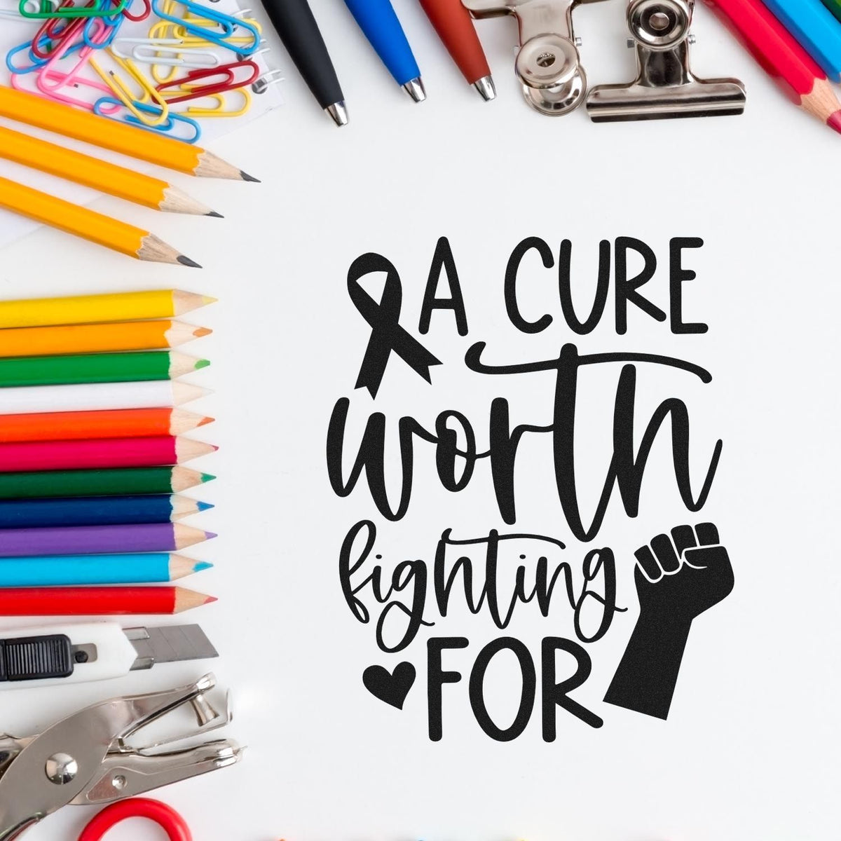 Black A Cure Worth Fighting For stamp, framed by colorful pencils, clips, pens, and metal seal tools.