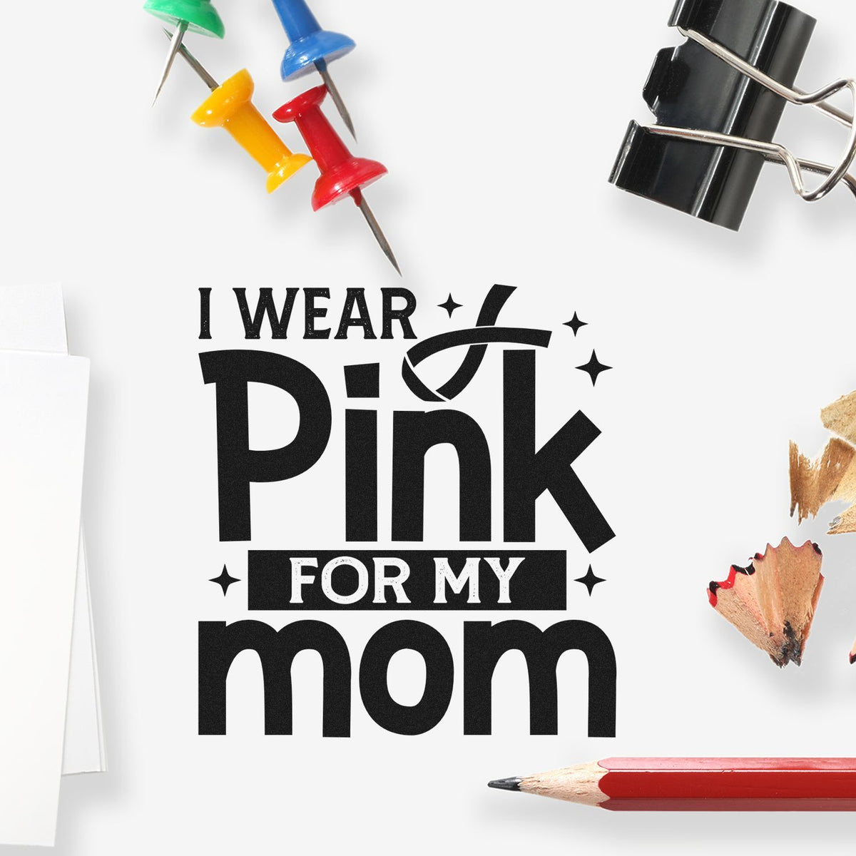 Custom stamp and seal design reading I wear pink for my mom, with black text, colorful push pins, binder clip, and red pencil.