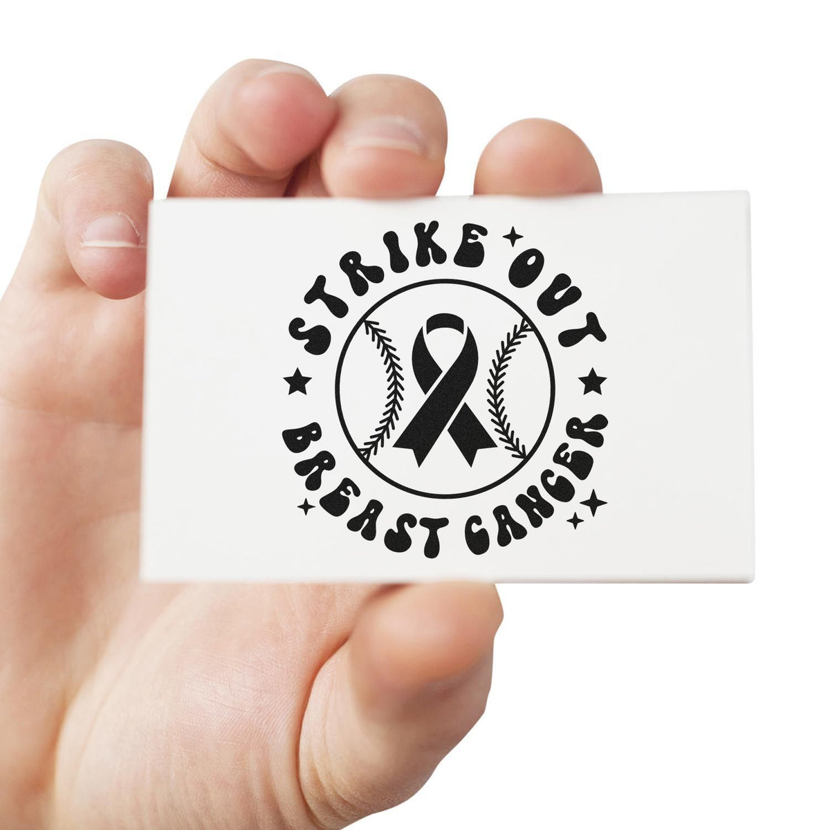 White stamp and seal block with black Strike Out Breast Cancer ribbon logo and baseball seams, held in hand.