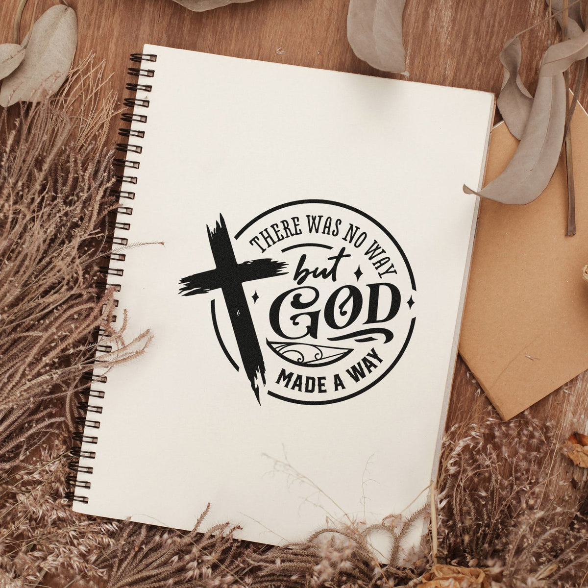 Black Christian stamp seal with cross and There Was No Way but God Made a Way on a cream spiral notebook, rustic brown decor.