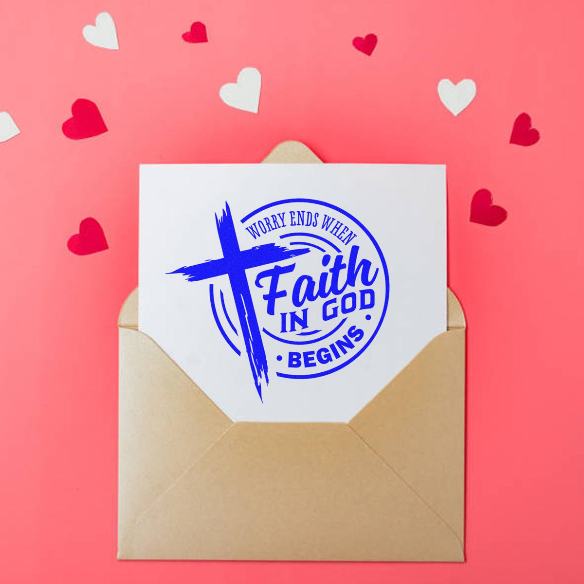 Christian faith stamp seal in blue on a white card, tucked in a tan envelope with heart confetti on a pink background.