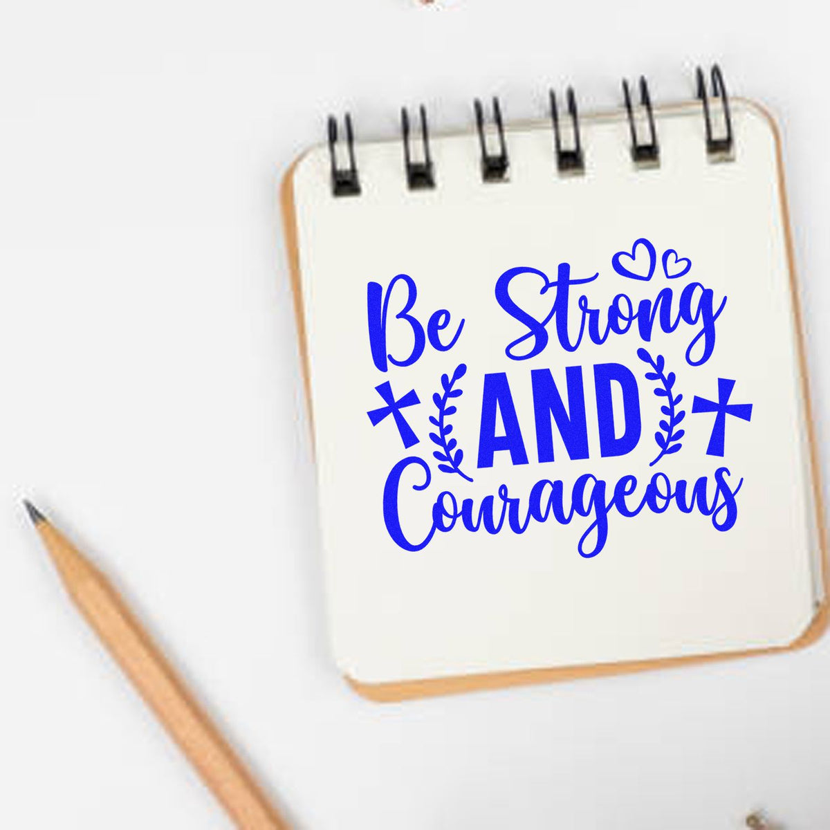 Blue custom stamp/seal design on cream notebook reading Be Strong and Courageous, with hearts and leaf accents.